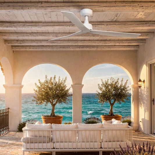 Ventilateur de plafond extérieur blanc MARINE installé sur une terrasse avec vue sur mer, plafonds en bois, mobilier blanc et plantes en pot.