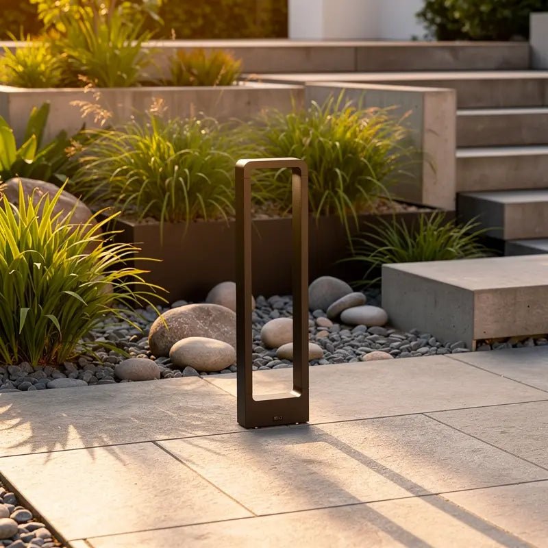 Borne extérieure design DAS-G noire, forme rectangulaire ouverte, installée sur terrasse pavée avec gravier et plantes décoratives.