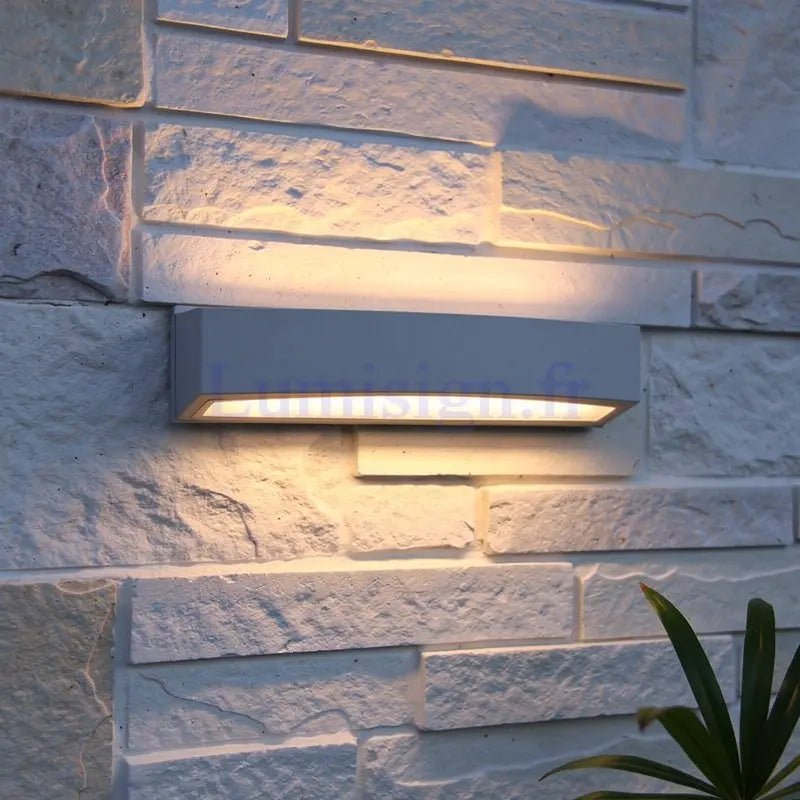 Applique extérieure moderne Andromeda de couleur anthracite fixée sur mur en pierre blanche, éclairage haut et bas