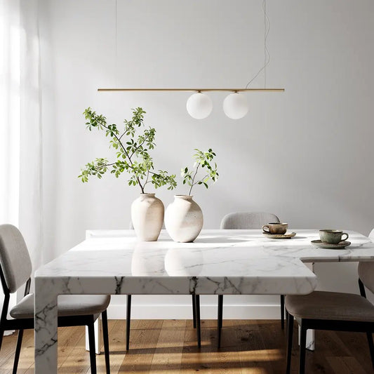 Suspension moderne PERLINE en laiton doré avec deux globes blancs au-dessus d’une table à manger en marbre