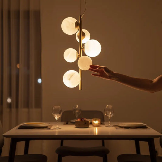 Suspension PERLAGE SP6 en laiton avec diffuseurs blancs; éclairage chaleureux au-dessus d’une table