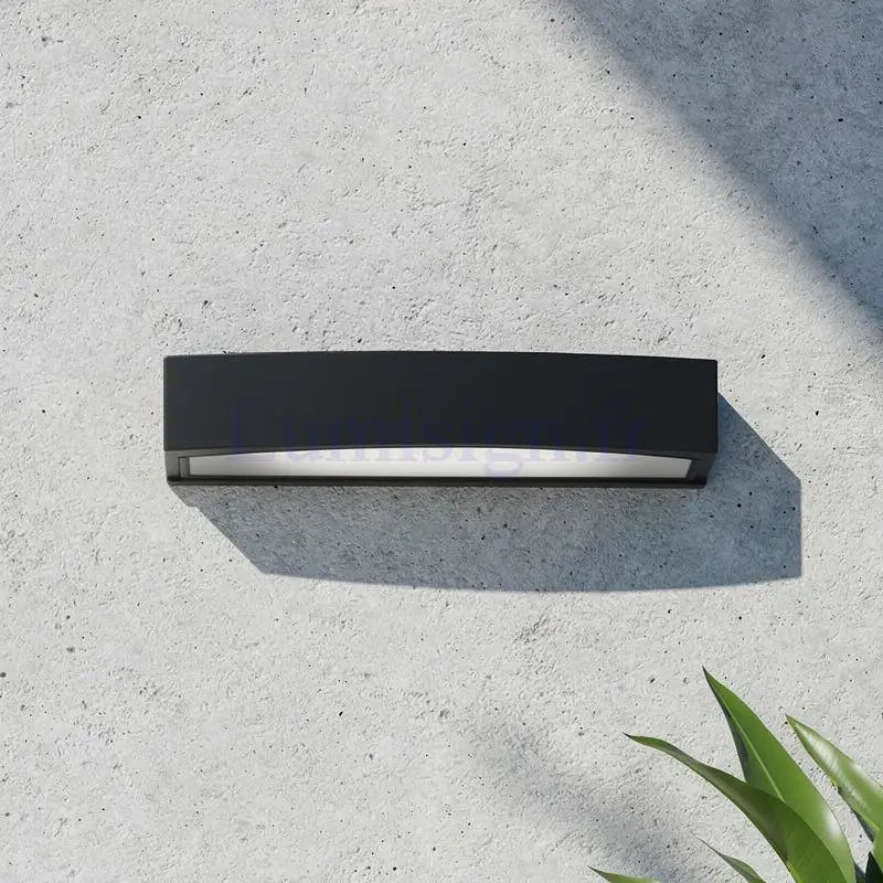 Applique extérieure Andromeda noire de forme rectangulaire galbée fixée sur mur en béton, éclairage haut et bas