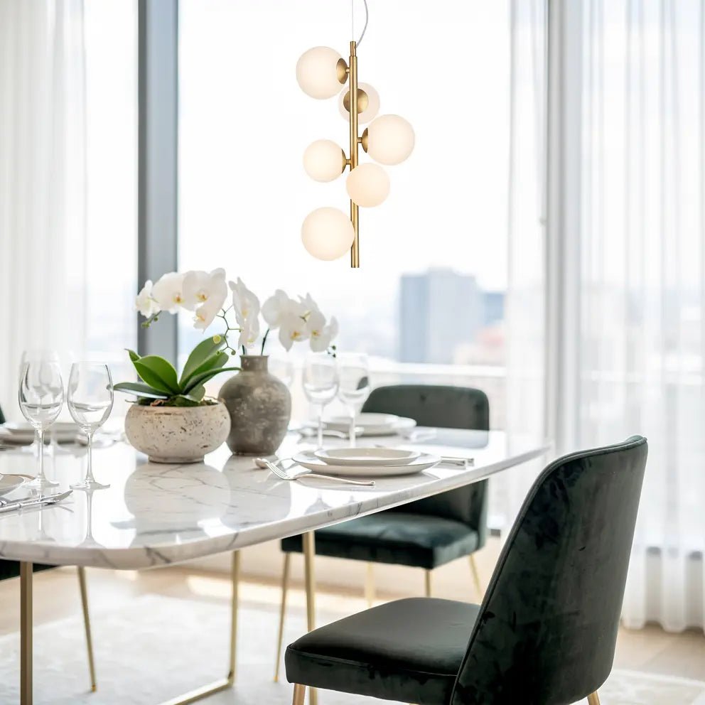 Lustre suspendu doré avec globes blancs au-dessus d’une table de dîner chic en marbre