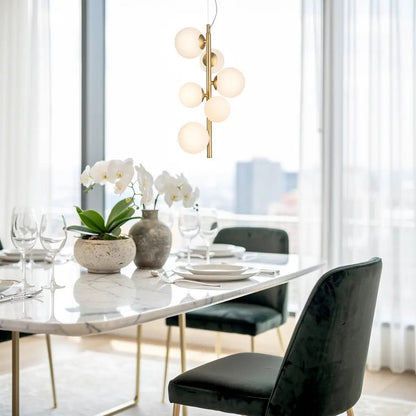 Lustre suspendu doré avec globes blancs au-dessus d’une table de dîner chic en marbre