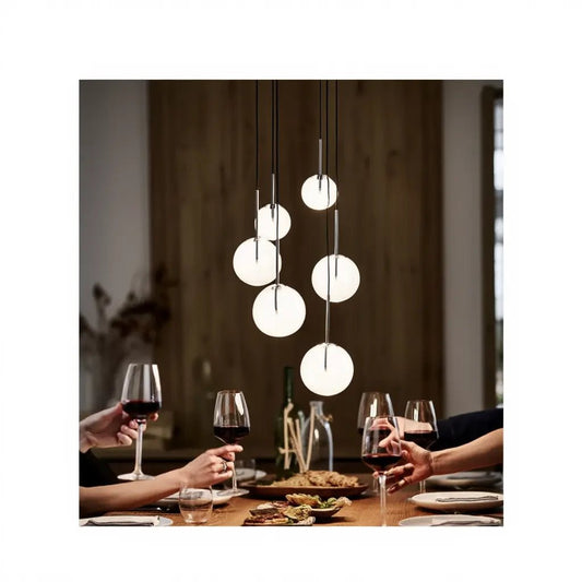 Suspension EQUINOXE : orbes lumineuses suspendues au-dessus d’une table de dîner avec verres de vin et plats, ambiance chaleureuse.