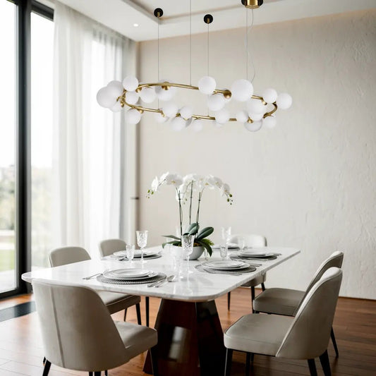 Suspension PERLAGE SP30 ovale dorée avec boules blanches suspendues au-dessus d'une table à manger blanche