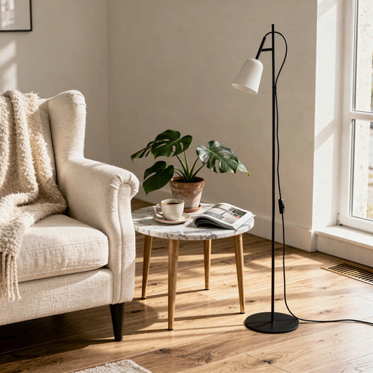 Lampadaire STUDIO noir à abat-jour blanc près d’un canapé beige, table ronde en marbre avec plante et tasse, ambiance cosy lumineuse.