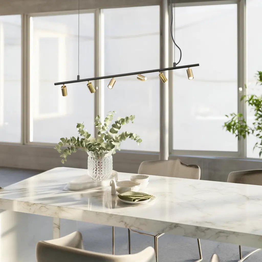 Suspension moderne DYNAMITE SP6 noire et laiton au-dessus d’une table en marbre, éclairant une salle lumineuse.