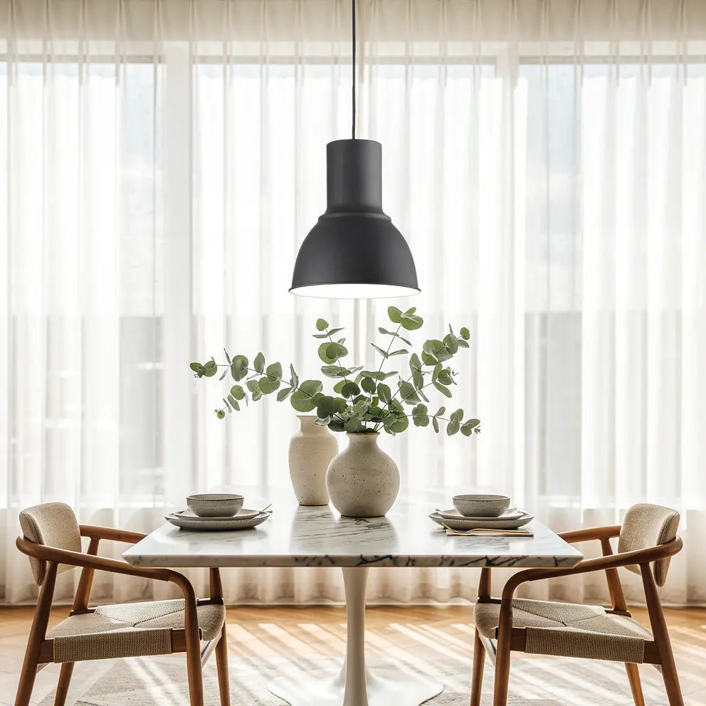 Suspension noire moderne au-dessus d’une table en marbre, vase et feuillage vert, assiettes et bols sur table