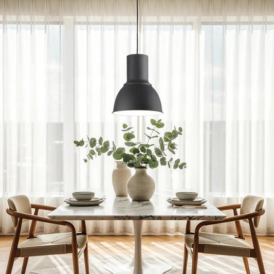 Suspension noire moderne au-dessus d’une table en marbre, vase et feuillage vert, assiettes et bols sur table