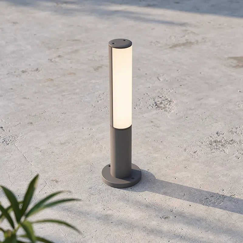 Lampe extérieure BERET-P, poteau lumineux gris avec abat-jour cylindrique éclairant, fixé sur socle rond sur terrasse en béton.