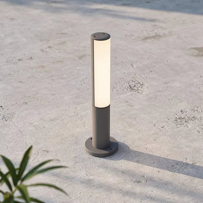 Lampe extérieure BERET-P, poteau lumineux gris avec abat-jour cylindrique éclairant, fixé sur socle rond sur terrasse en béton.